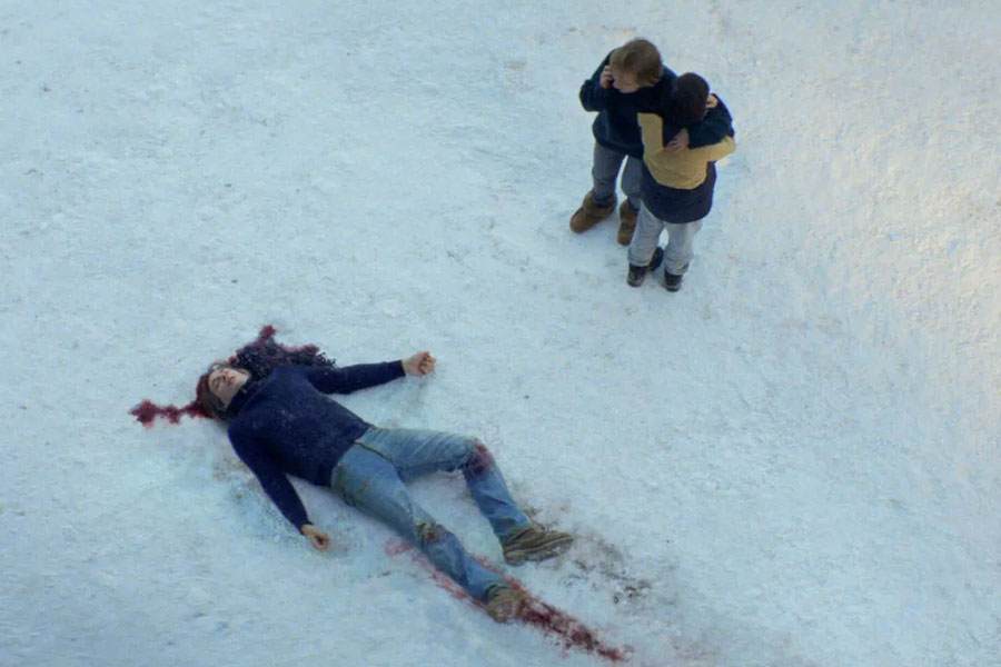 Anatomia de uma queda. Um homem caido sobre a neve manchada com seu sangue é observado pela esposa que segura seu filho com o rosto voltado para tras